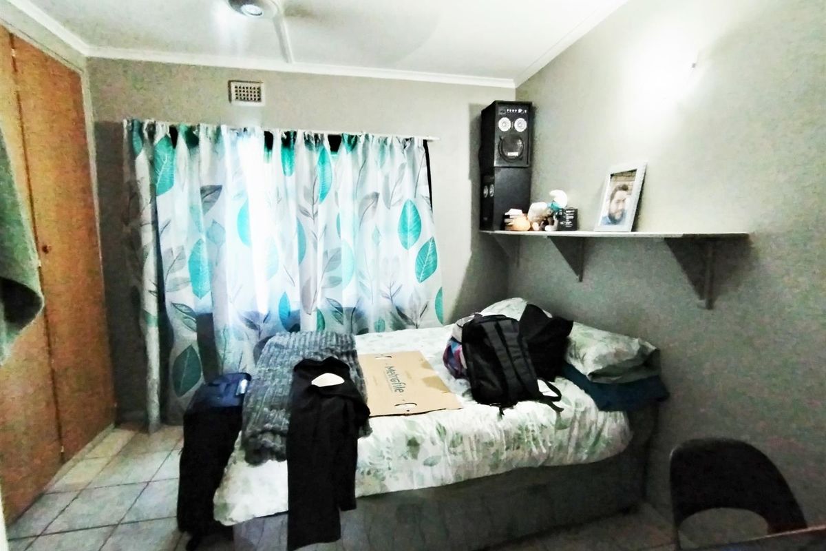 A functional bedroom featuring tiled flooring, a built-in cupboard, and a ceiling fan, providing a practical living space.