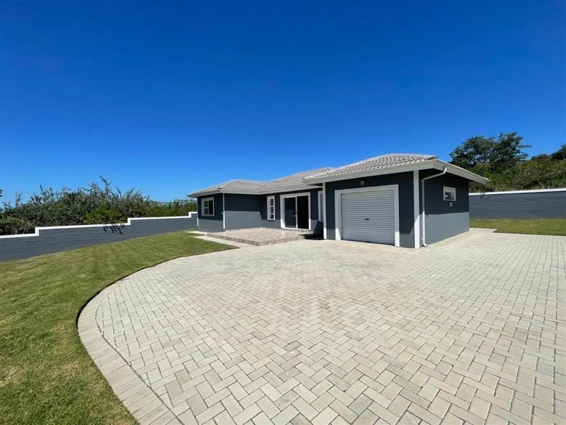A well-maintained single-story house featuring a paved driveway, attached garage, and a clean exterior finish with a surrounding boundary wall.