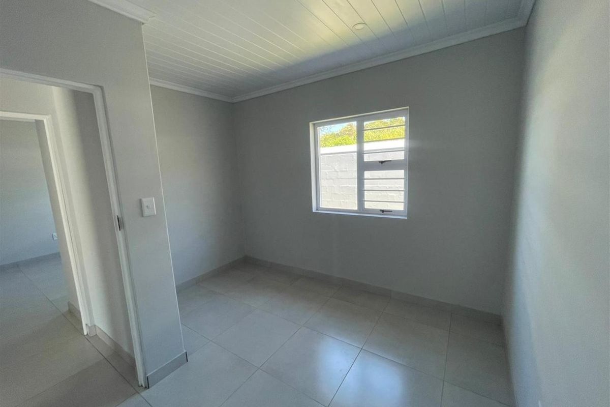 A clean, vacant bedroom featuring neutral tiled flooring, a white tongue and groove ceiling, and a single window providing natural light.