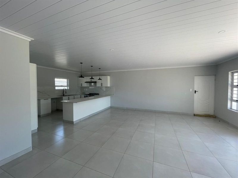 Spacious open-plan living area featuring a modern kitchen with a breakfast island, tiled flooring, and a clean, neutral aesthetic.