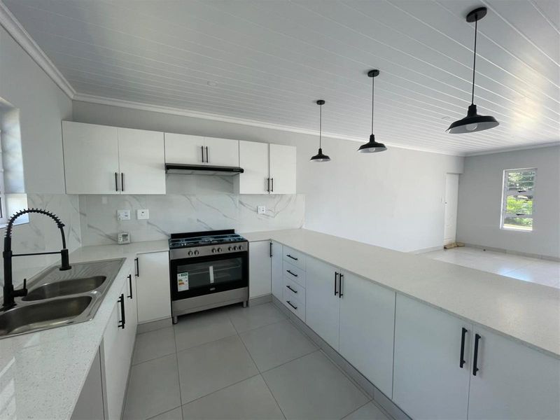 Modern open-plan kitchen featuring white cabinetry, stone countertops, marble-look splashback, and high-quality stainless steel appliances with contemporary pendant lighting.