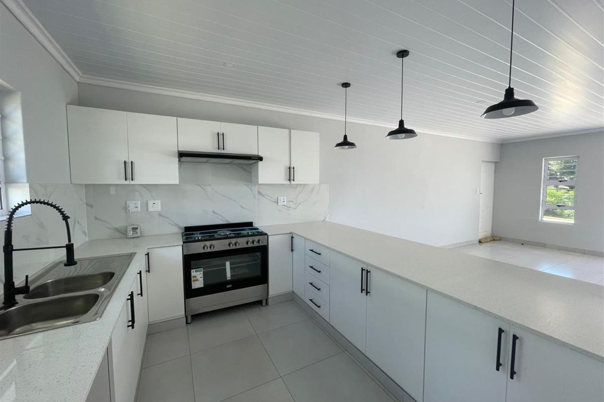 Modern open-plan kitchen featuring white cabinetry, stone countertops, marble-look splashback, and high-quality stainless steel appliances with contemporary pendant lighting.