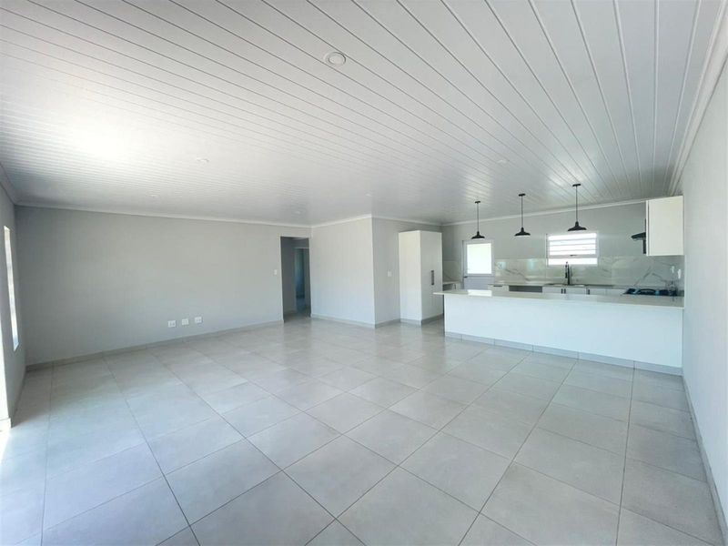 Spacious open-plan living area featuring large format floor tiles, a modern kitchen with stone countertops, and a clean, minimalist aesthetic.