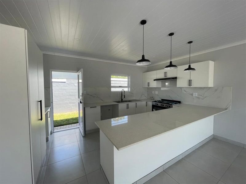 Modern kitchen featuring white cabinetry, quartz countertops, marble-look splashback, gas stove, and pendant lighting, with direct access to the rear garden.