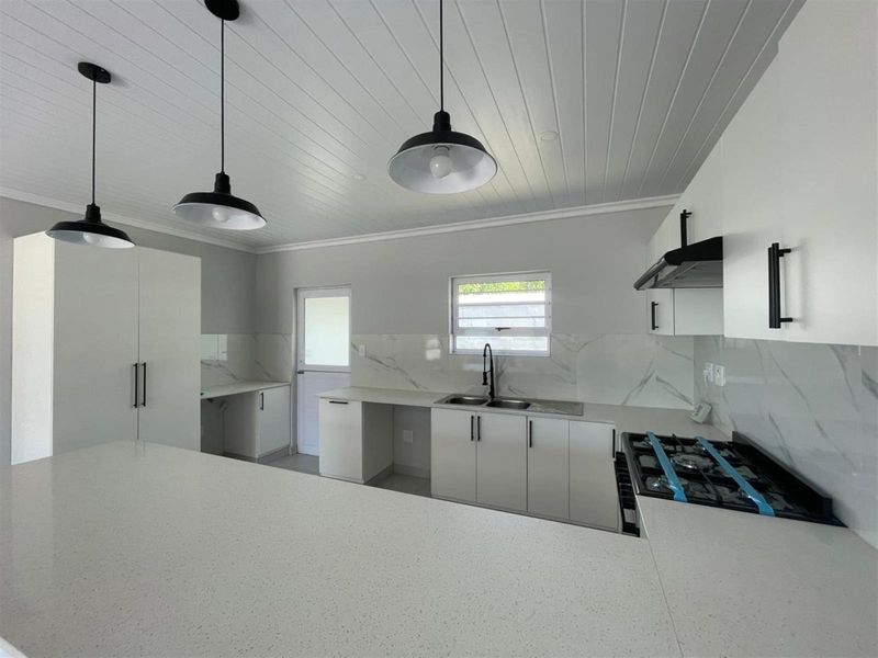 Modern, newly renovated kitchen featuring white shaker cabinetry, quartz countertops, a gas hob, and a stylish marble-look splashback with contemporary pendant lighting.
