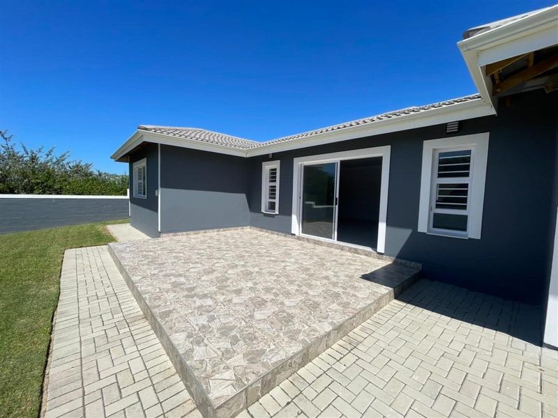 A well-maintained rear exterior view featuring a tiled patio, paved walkways, and a modern sliding door entrance to the home.