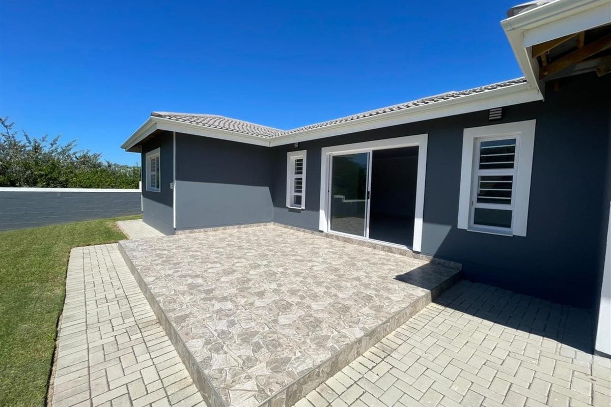 A well-maintained rear exterior view featuring a tiled patio, paved walkways, and a modern sliding door entrance to the home.