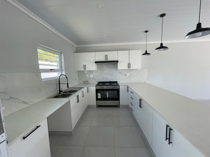 Modern kitchen featuring white cabinetry, stone countertops, marble-look splashback, and a freestanding gas stove with an extractor fan.