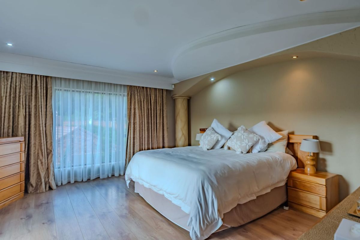 Spacious bedroom featuring a decorative arched ceiling detail, recessed lighting, and large windows with floor-to-ceiling curtains, finished with wood-look flooring.
