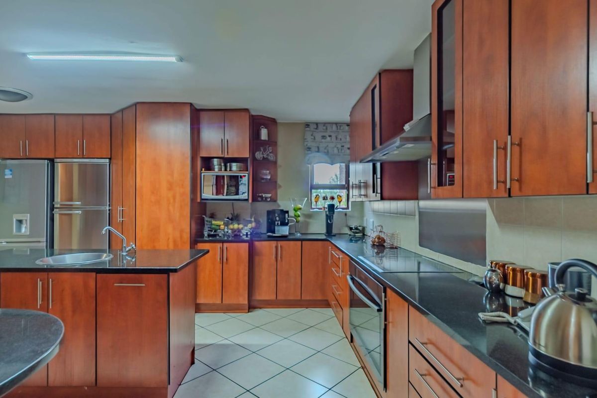 A functional kitchen featuring warm-toned wooden cabinetry, dark granite countertops, a central island with a sink, and integrated stainless steel appliances.