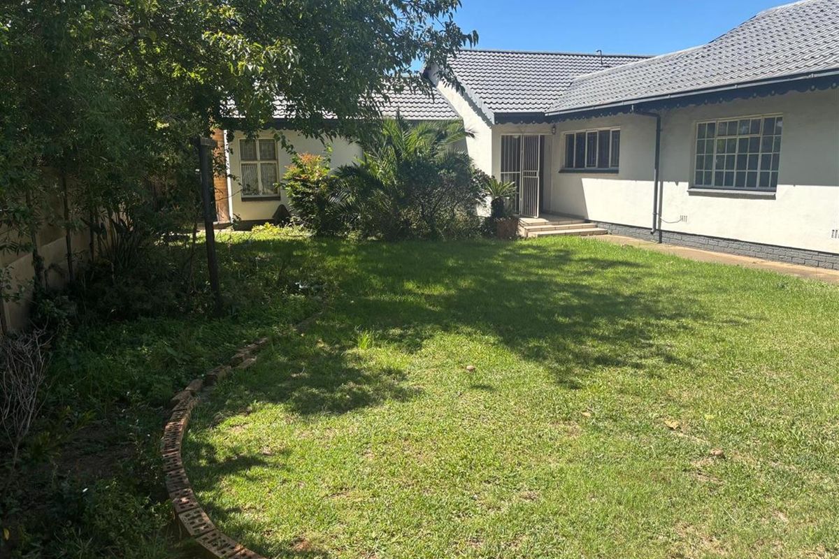 A view of the rear garden and back elevation of the house, featuring a lawn area and established trees.