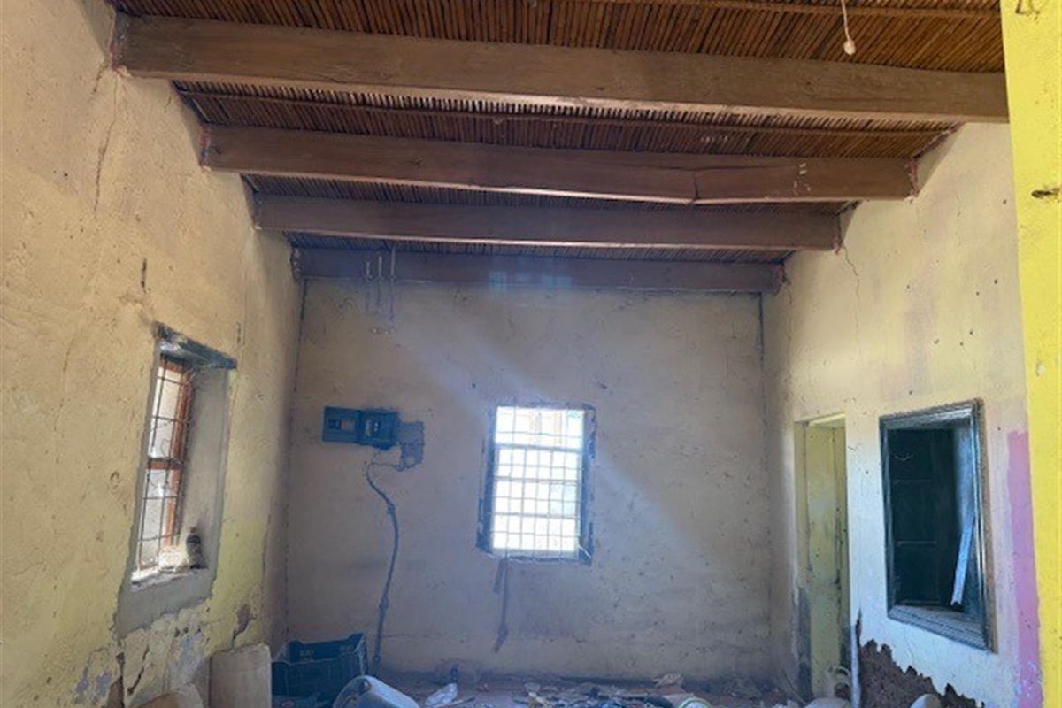 An interior view of a room in poor condition, featuring exposed timber beams, a reed ceiling, and significant wall damage requiring extensive renovation.