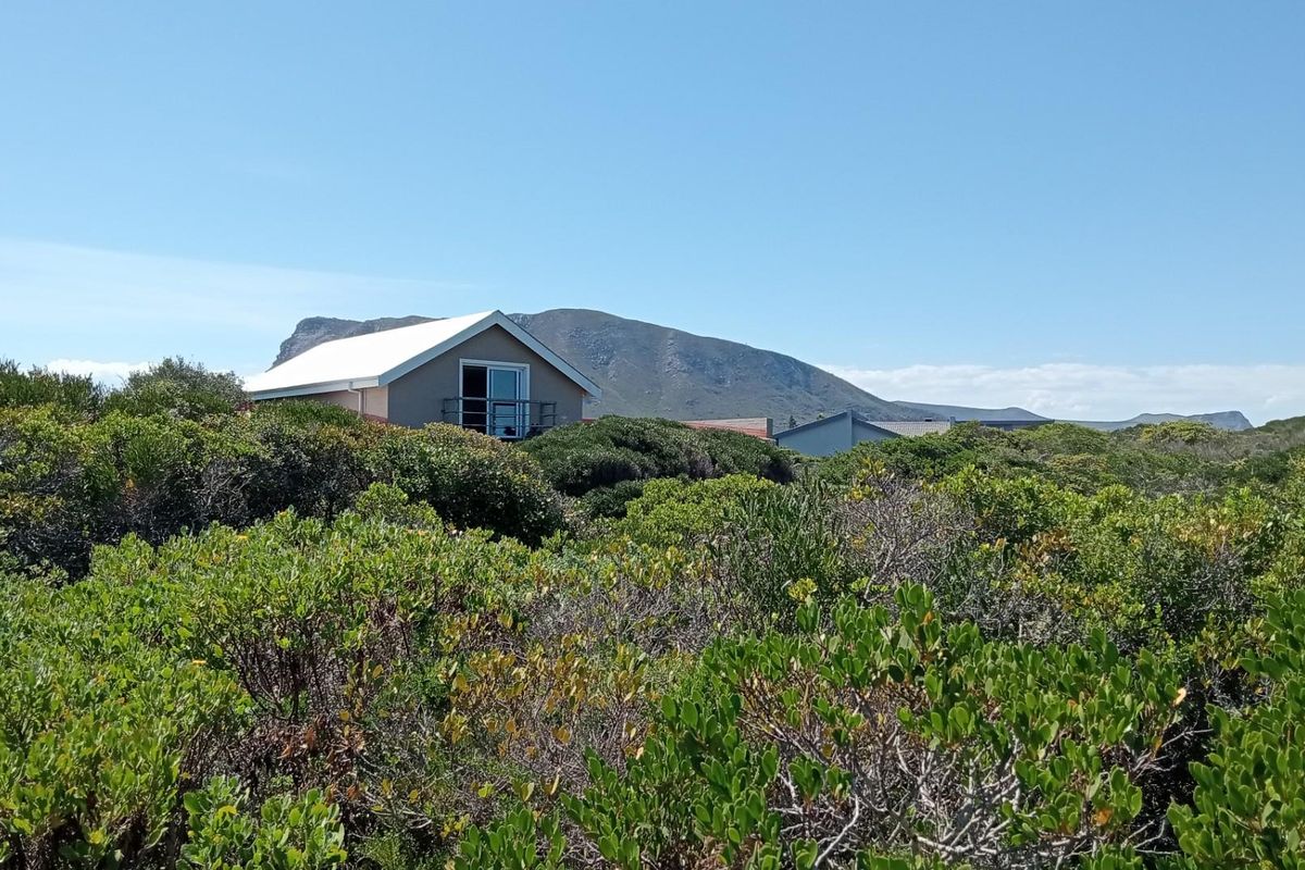 A view of the rear elevation of a residential property nestled within natural coastal vegetation, featuring a balcony and mountain backdrop.