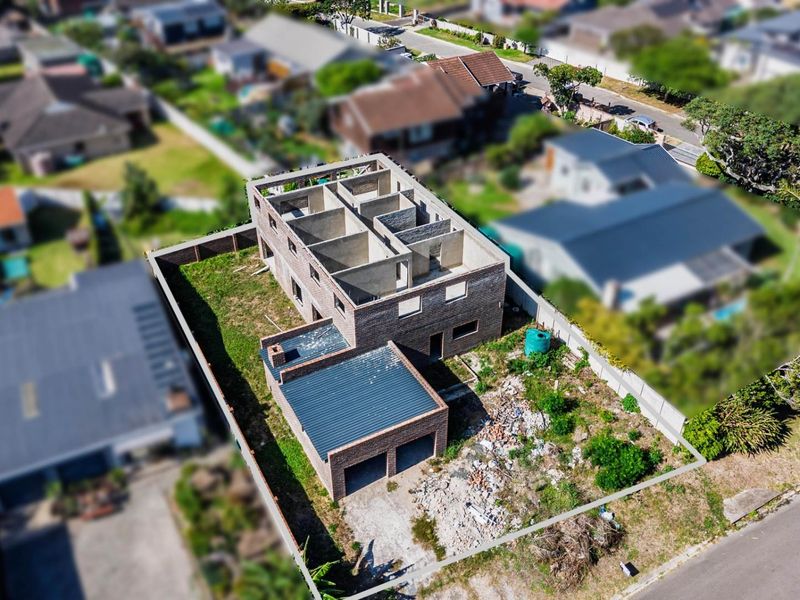 Aerial view of a residential property under construction, featuring a double garage and an unfinished multi-level brick structure on a fenced plot.