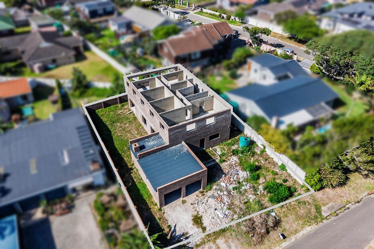 Aerial view of a residential property under construction, featuring a double garage and an unfinished multi-level brick structure on a fenced plot.