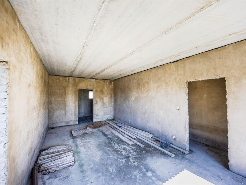 An unfinished interior room in shell condition, featuring raw concrete walls, flooring, and ceiling, offering a blank canvas for complete renovation.
