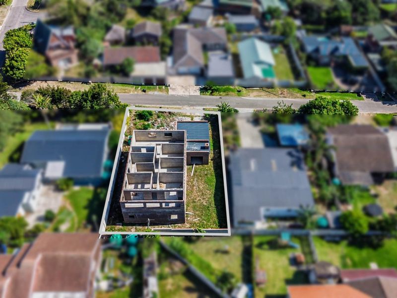Aerial view of a residential property currently under construction, showing the concrete shell and foundation layout on a fenced plot.