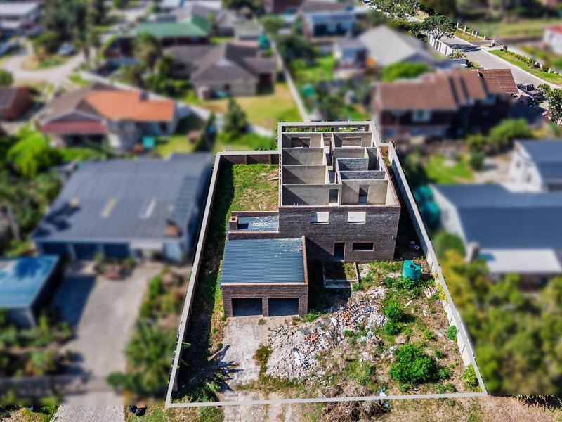 Aerial view of a residential property under construction, featuring a double garage and an unfinished two-story brick structure on a large plot.