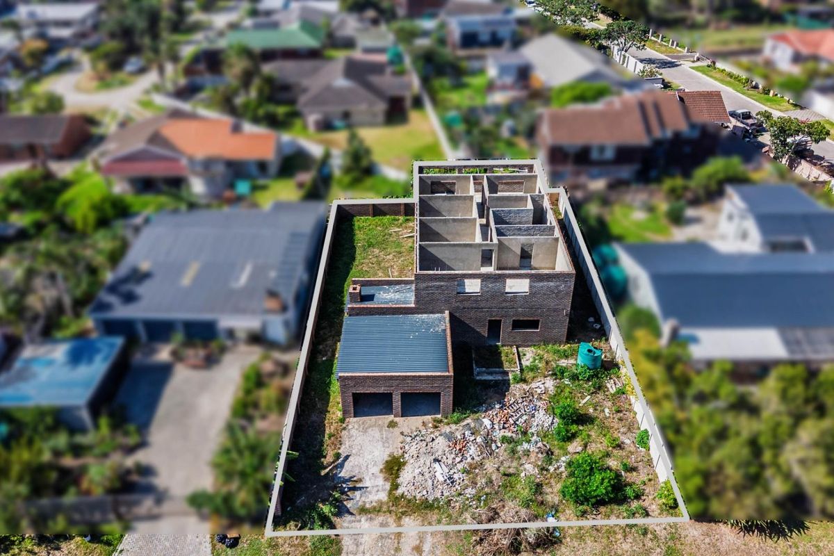 Aerial view of a residential property under construction, featuring a double garage and an unfinished two-story brick structure on a large plot.
