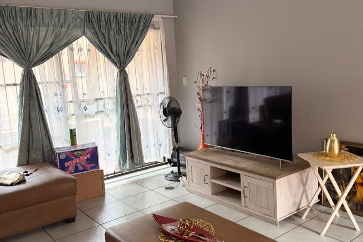 A living room featuring tiled flooring and a sliding glass door with security gate, providing access to the exterior.