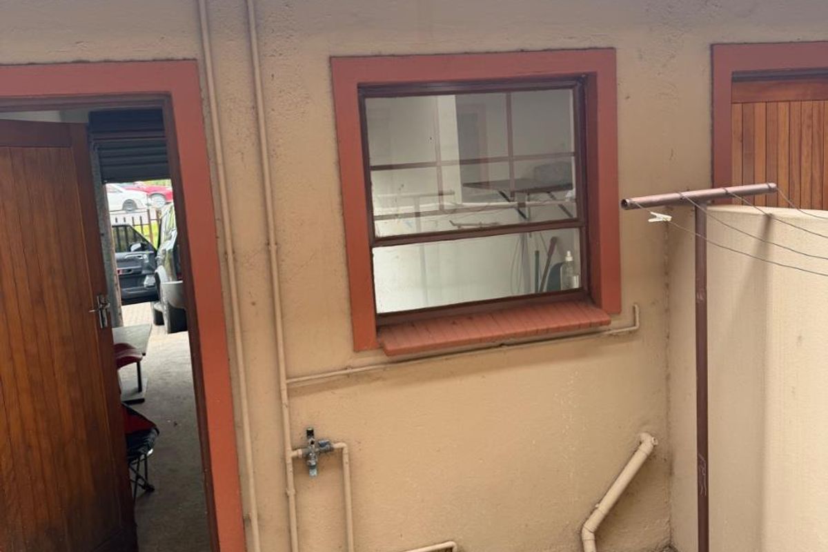 Rear exterior view of the apartment featuring a paved courtyard, external plumbing, and access door.