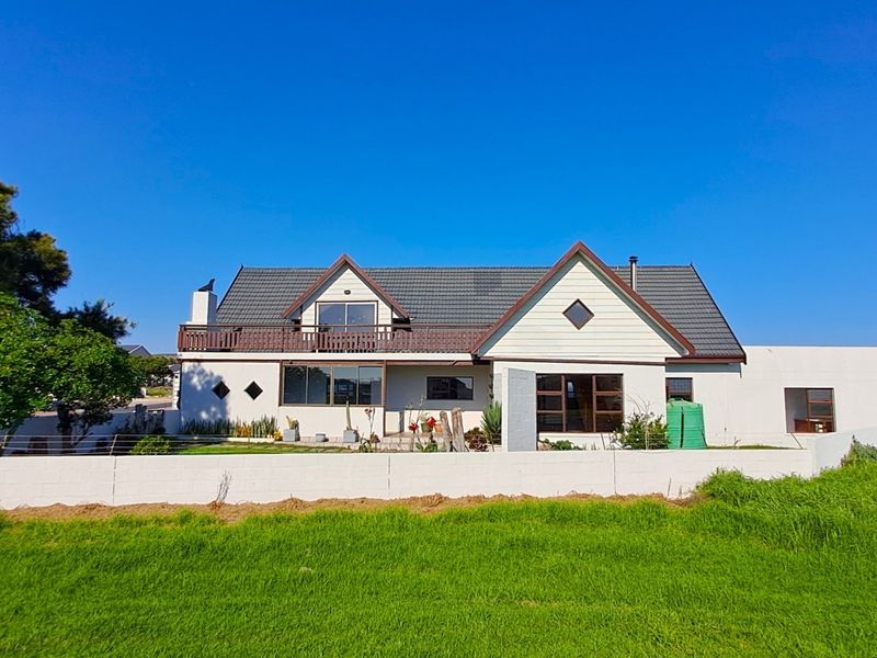 A detached house featuring a tiled roof, upper-level balcony, and a perimeter boundary wall, set within a spacious garden area.