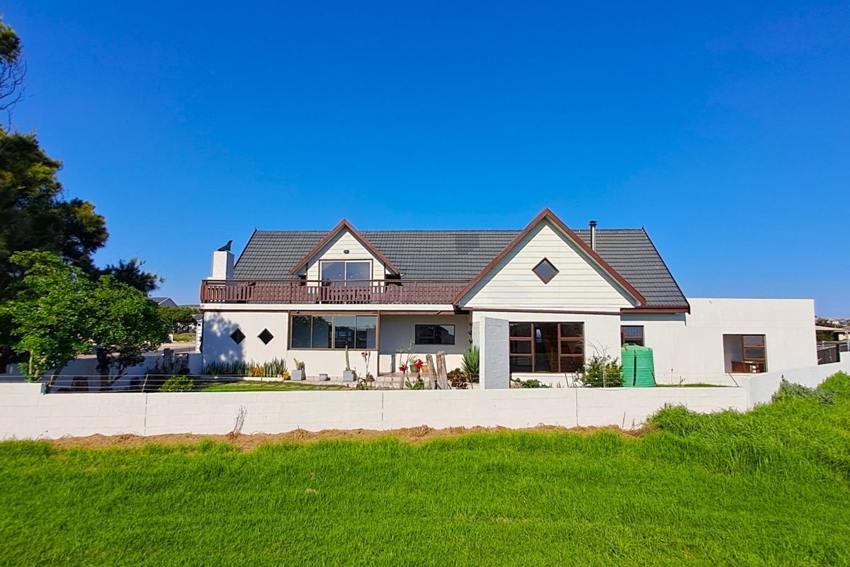 A detached house featuring a tiled roof, upper-level balcony, and a perimeter boundary wall, set within a spacious garden area.