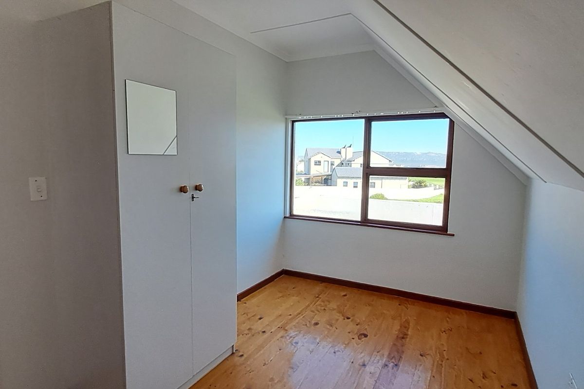 A bedroom featuring timber flooring, built-in cabinetry, and a sloped ceiling with a window offering neighbourhood views.
