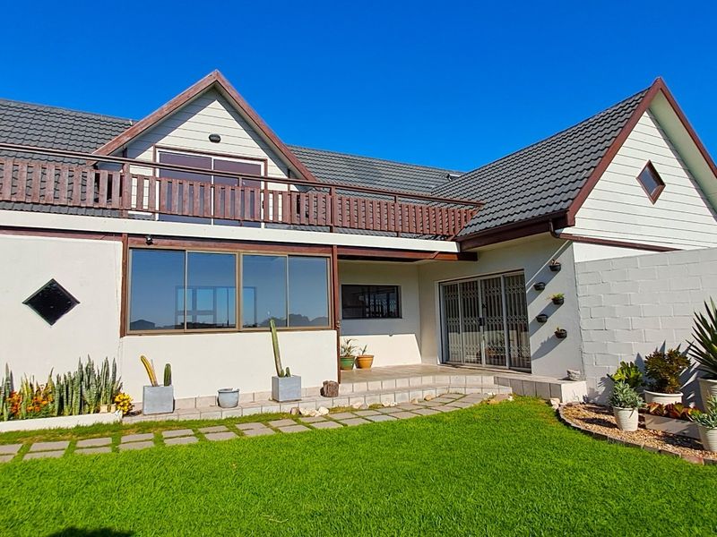 Rear view of the house featuring a tiled roof, upper-level balcony with wooden railing, and a paved patio area leading to the garden.