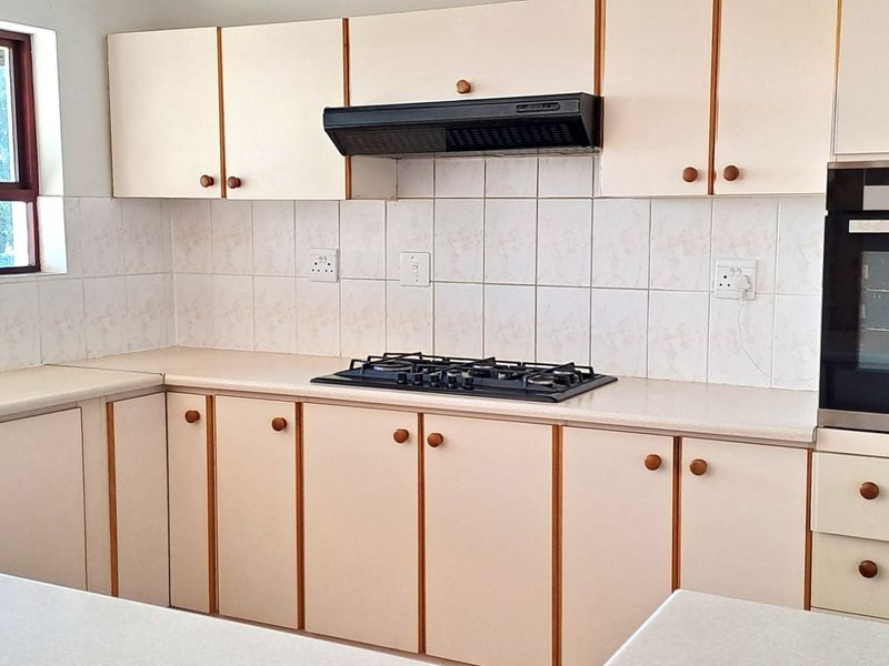 A functional kitchen featuring light-toned cabinetry, built-in oven, gas hob, extractor fan, and tiled splashbacks with a stainless steel sink.