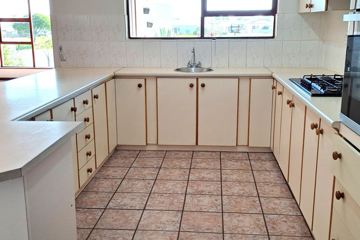 A functional kitchen featuring U-shaped cabinetry, a built-in oven, gas hob, and tiled flooring, with an adjacent living area visible in the background.