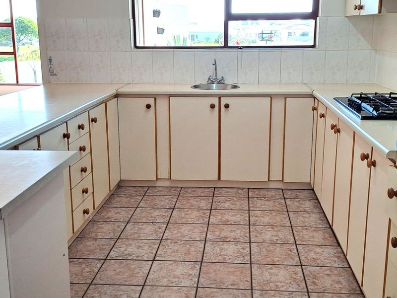 A functional kitchen featuring U-shaped cabinetry, a built-in oven, gas hob, and tiled flooring, with an adjacent living area visible in the background.