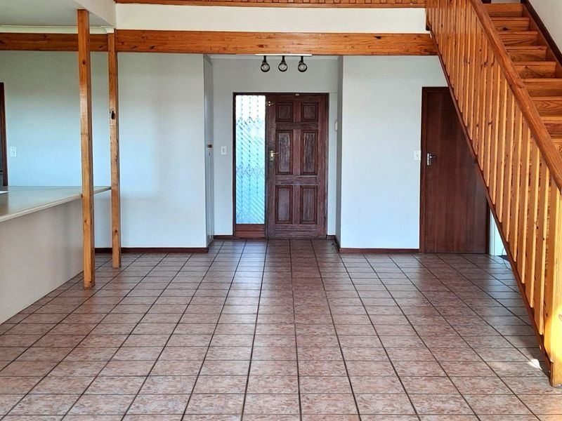 Spacious open-plan living area featuring tiled flooring, a timber staircase, and a wooden front entrance door.