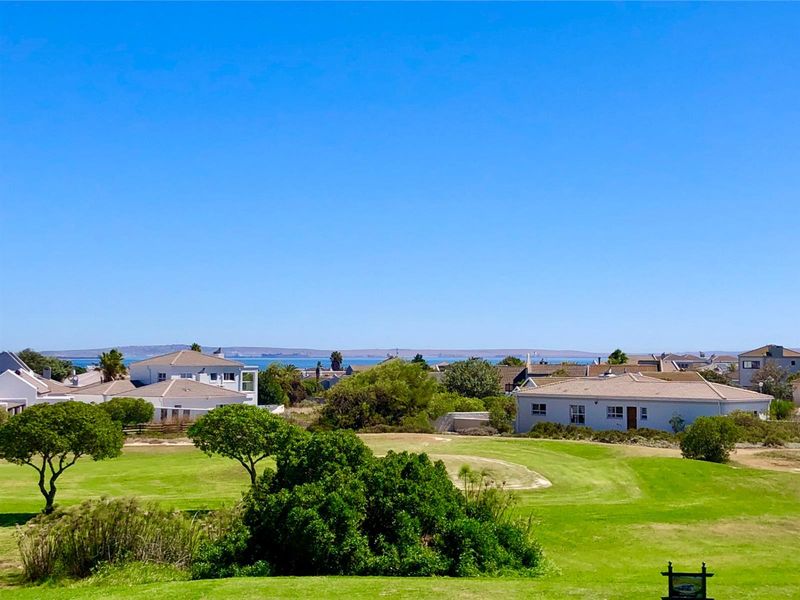 A scenic elevated view overlooking a lush green golf course with surrounding residential properties and a distant ocean horizon.