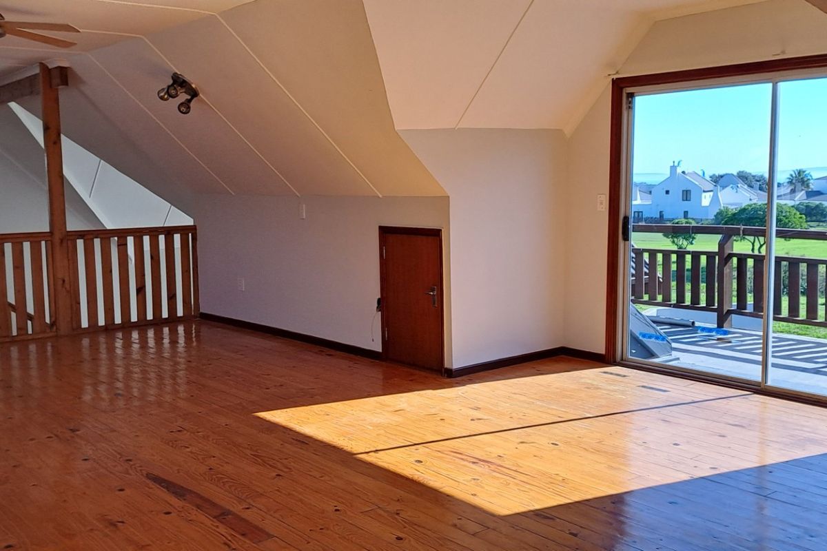 Spacious attic-style living area featuring polished timber flooring, vaulted ceilings, and sliding glass doors opening onto a balcony with scenic views.