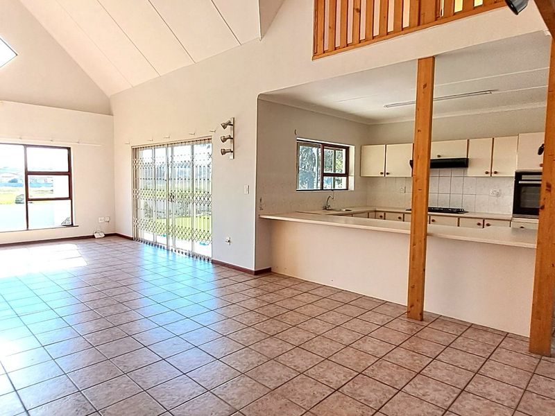 Spacious open-plan living area featuring high vaulted ceilings, tiled flooring, and a functional kitchen with built-in oven and breakfast bar.