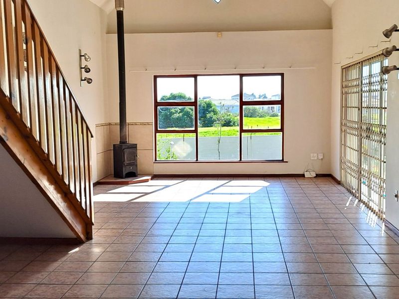Spacious open-plan living area featuring tiled flooring, a wood-burning fireplace, and a staircase leading to the upper level.