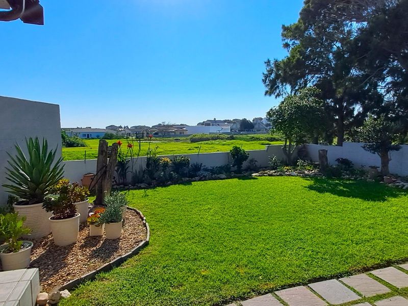 A well-maintained rear garden featuring a manicured lawn, paved pathway, and perimeter wall, offering pleasant views of the surrounding landscape.