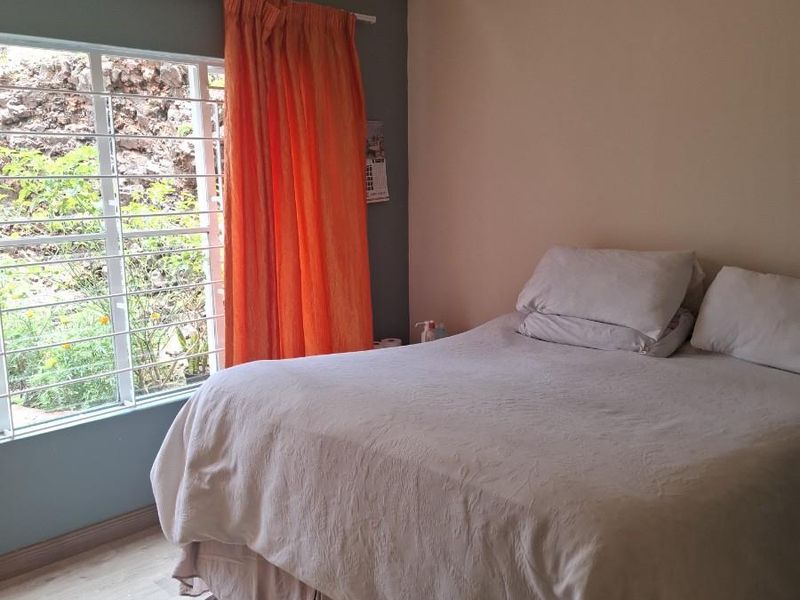 A bedroom featuring light-toned flooring, a window with security bars, and an accent wall.