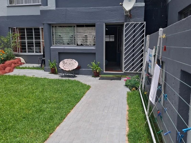 Ground floor apartment exterior featuring a paved walkway, private garden area, and secure metal security gate at the entrance.