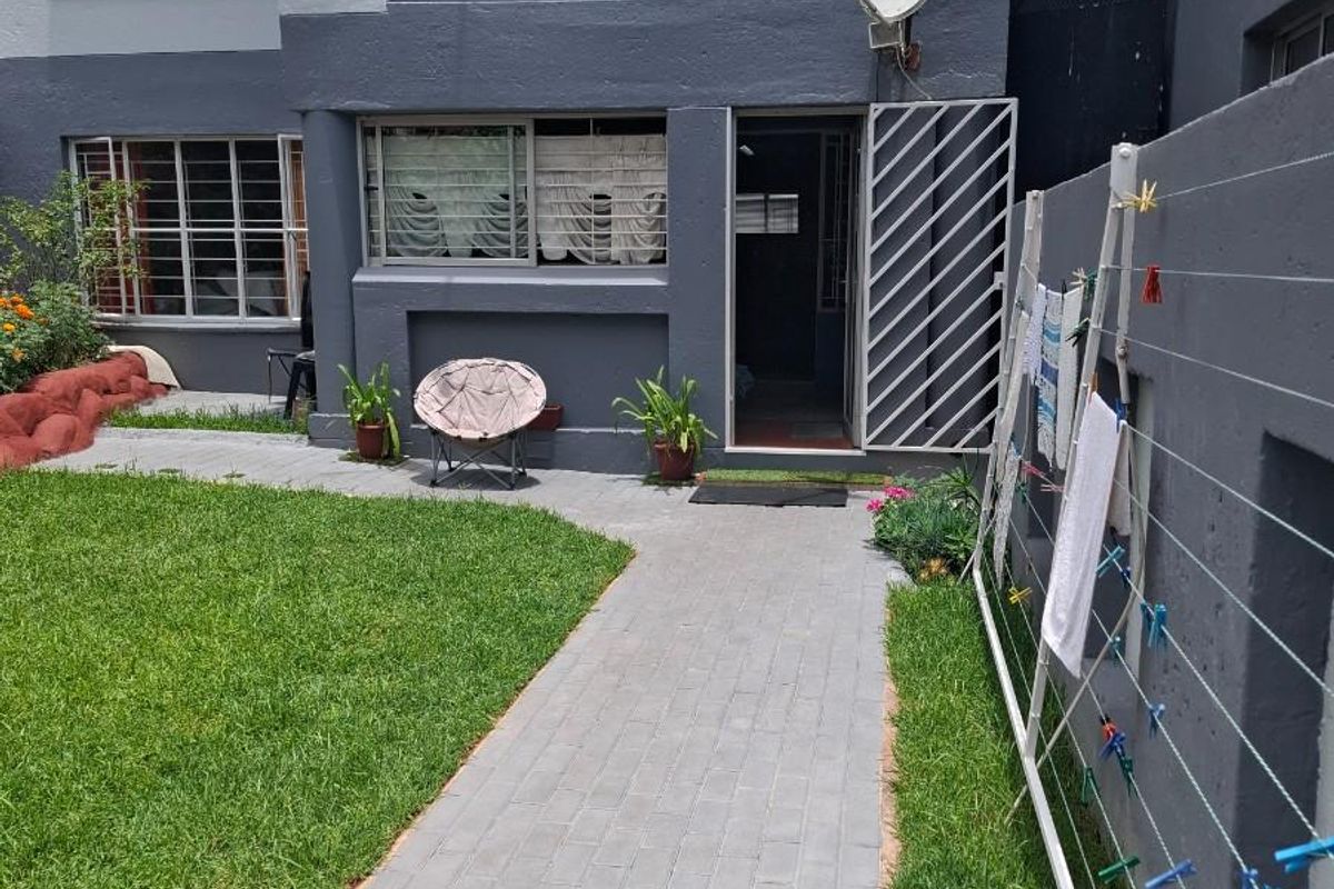 Ground floor apartment exterior featuring a paved walkway, private garden area, and secure metal security gate at the entrance.
