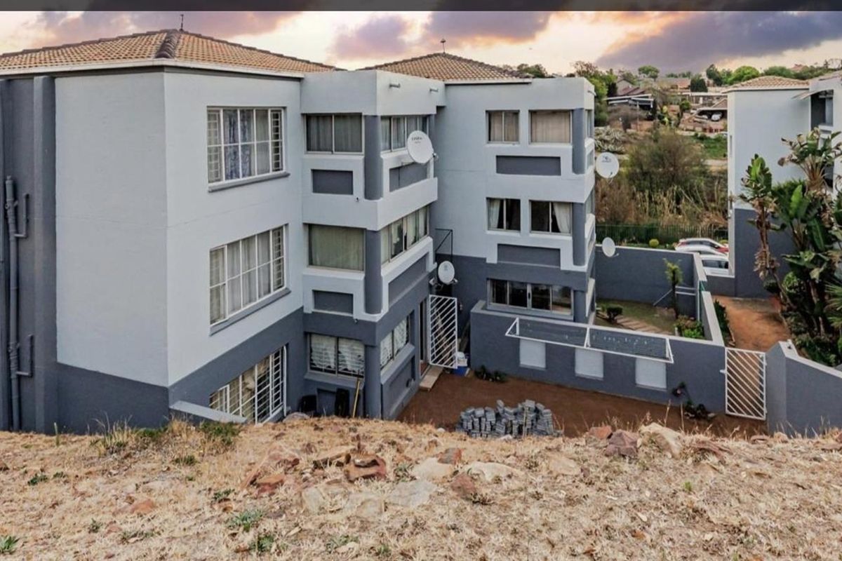 An elevated view of the apartment complex exterior, featuring multi-story residential blocks with grey and white facade finishes and surrounding grounds.