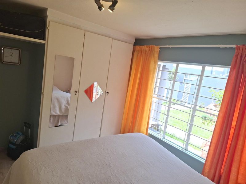 A bedroom featuring built-in white wardrobes with integrated mirrors and a large window with security bars overlooking the exterior grounds.