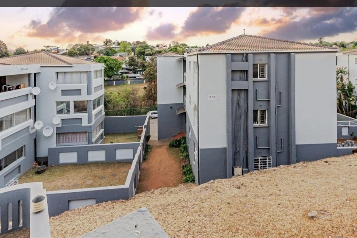 An elevated aerial view of a multi-story apartment complex featuring modern grey and white exterior facades, tiled roofing, and surrounding landscaped grounds.