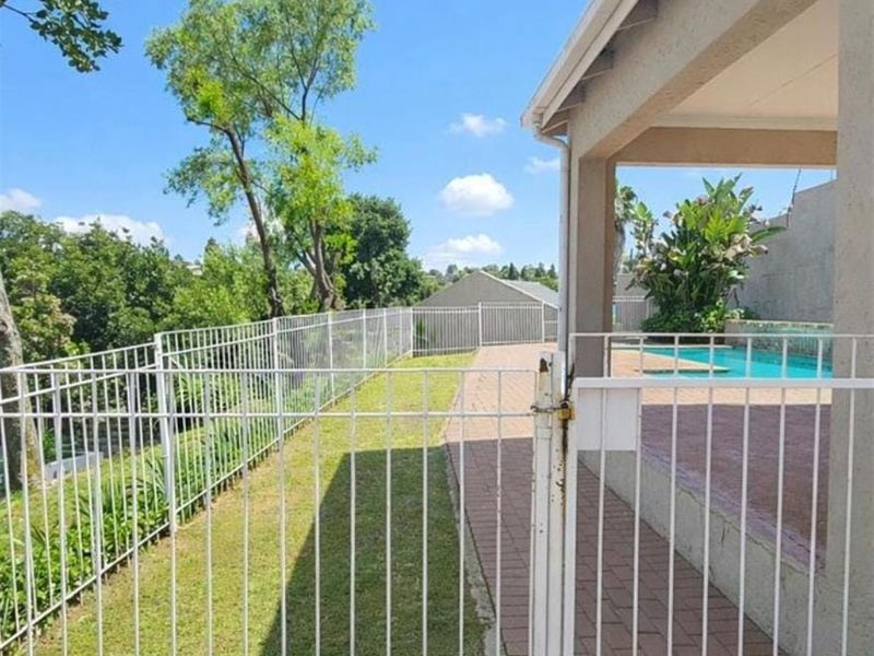 Outdoor area featuring a swimming pool, paved patio, and lawn enclosed by white metal fencing.