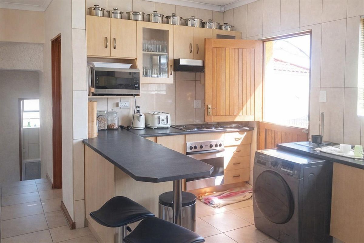 Compact kitchen featuring light wood cabinetry, dark countertops, built-in oven with hob, extractor fan, and integrated laundry appliance space.