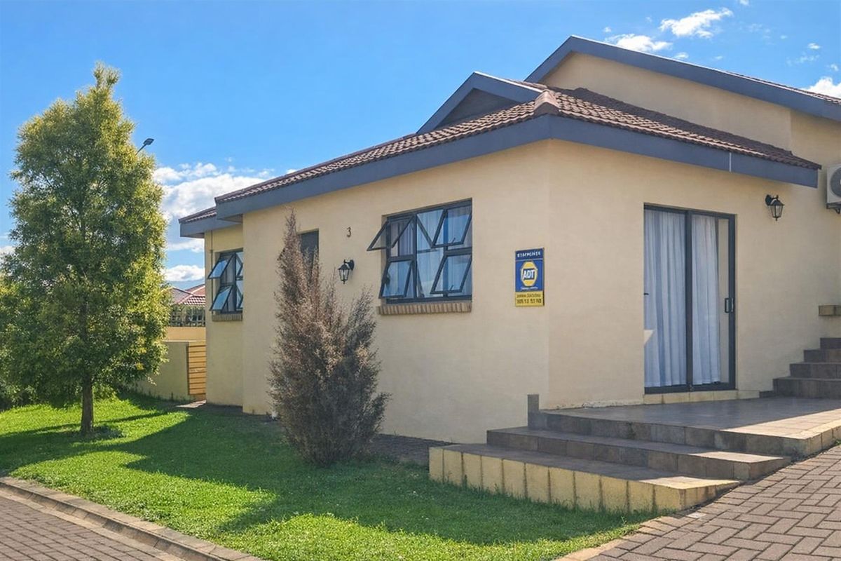 Exterior view of a townhouse featuring a tiled roof, paved entrance steps, and aluminium-framed windows, set within a well-maintained residential complex.
