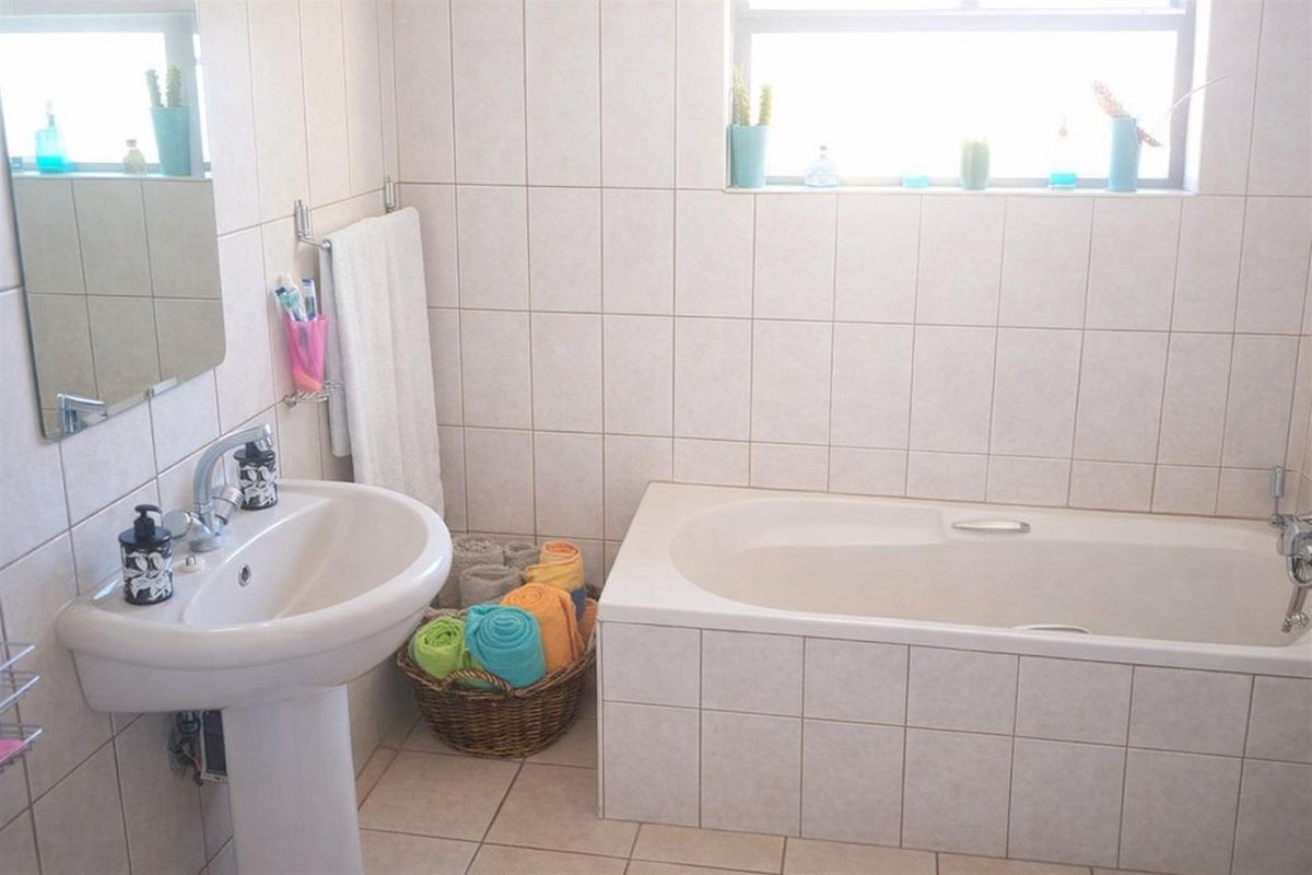 A functional bathroom featuring a pedestal sink, a tiled bathtub, and neutral wall and floor tiling with natural light from a window.