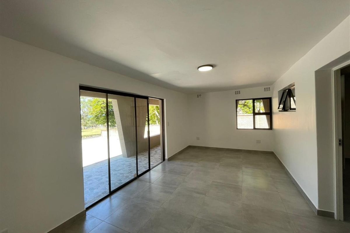 A bright, empty living room featuring large sliding glass doors leading to an outdoor area, neutral tiled flooring, and modern aluminium window frames.