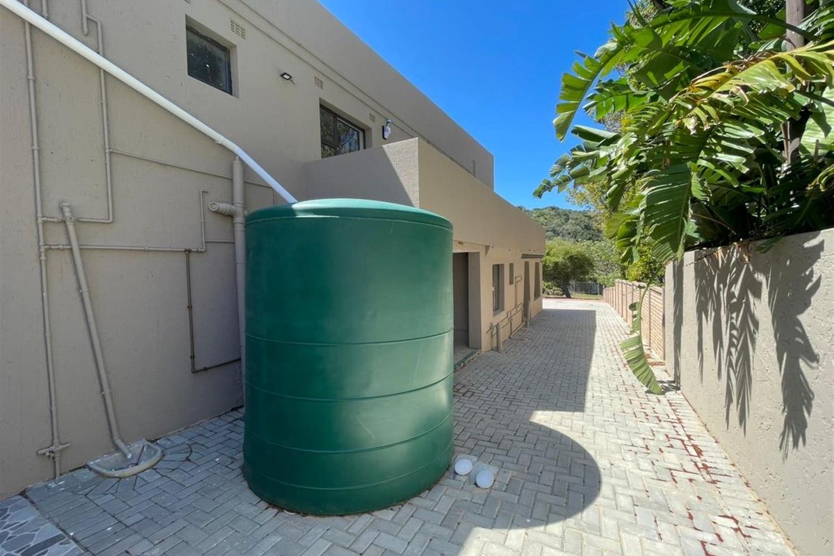 Rear exterior area featuring a large water storage tank, paved ground surface, and exterior building plumbing.